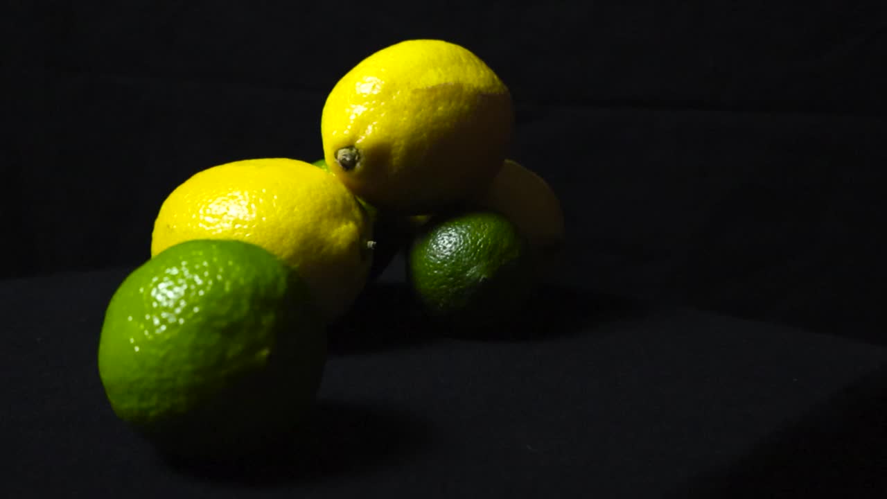 Gorgeous colorful and vibrant close up or closeup footage of yellow lemon and green lime fruit on a dark studio black background while footage is slowly zooming in on the healthy fruit with vitamins.