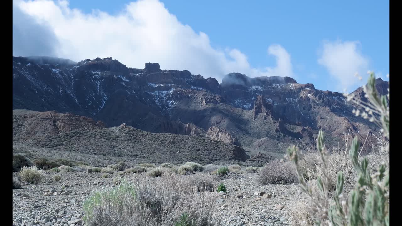 Paesaggio vulcanico arido con nuvole che si muovono sopra montagne innevate