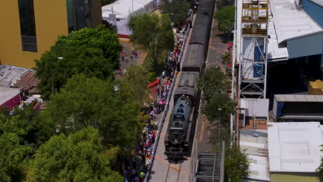 drone pulling out the scene of empress historic steam locomotive, the 2816, touring through a lush, urban area, fans gather, celebrating a ceremonial final spike linking canada, the u.s., and mexico