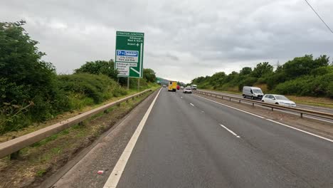 a yellow ambulance travels along a dual carriageway outside durham, england, under overcast daylight. the camera moves smoothly forward, capturing roadside signs and passing vehicles