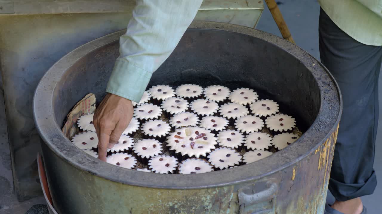 Baker touching Khanom Farang Kudeejeen cupcakes in tandoor-like oven with his finger