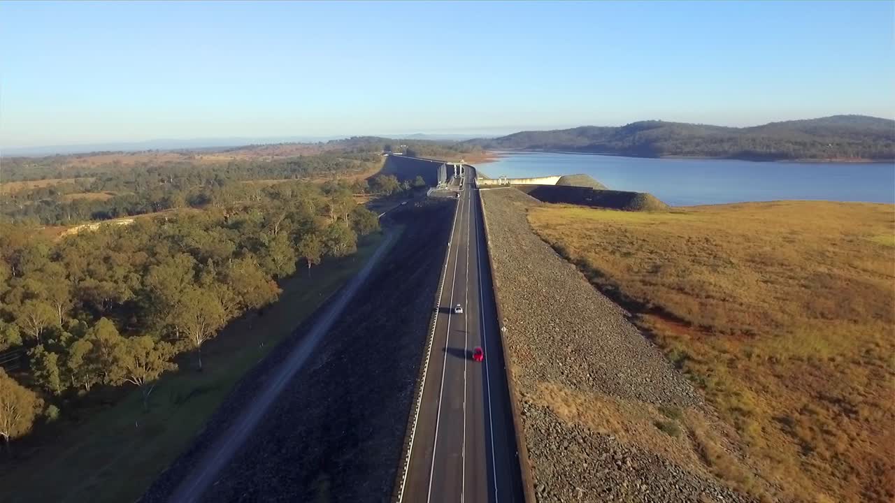 toma aérea volando a lo largo de la carretera hacia la presa wivenhoe, con el sol en un ángulo bajo, en el lago wivenhoe en la región de somerset de queensland
