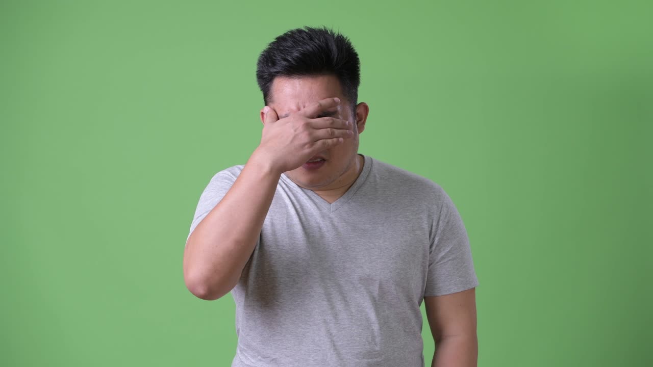 Young handsome overweight Asian man against green background