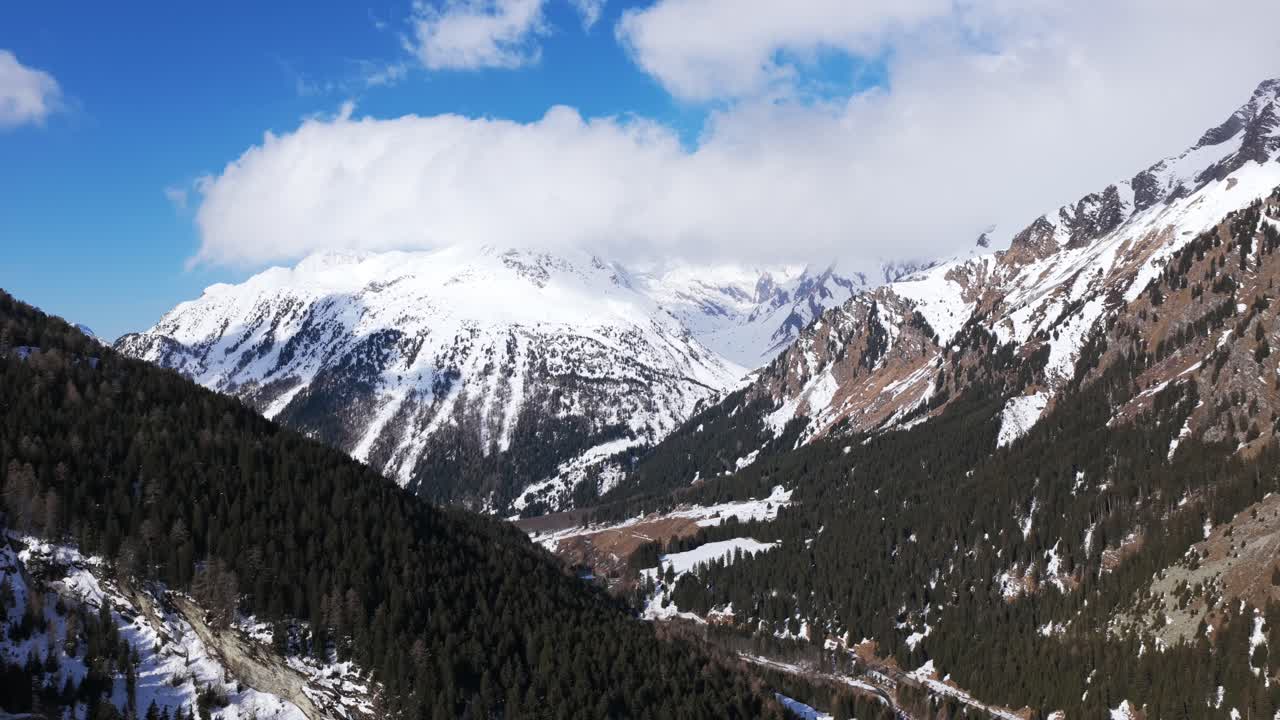 Maloja Pass, snow-covered mountains, pine forests, clouds obscuring peaks, winter landscapes, Switzerland. Aerial drone lateral view