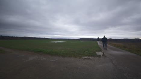modern black male waiting in open field under grey sky, europe, 4k | muscular, intimidating, shadow, figure, blurry, dark clothes, powerful, blurry, distant walk, puddle, thought, thinking, searching
