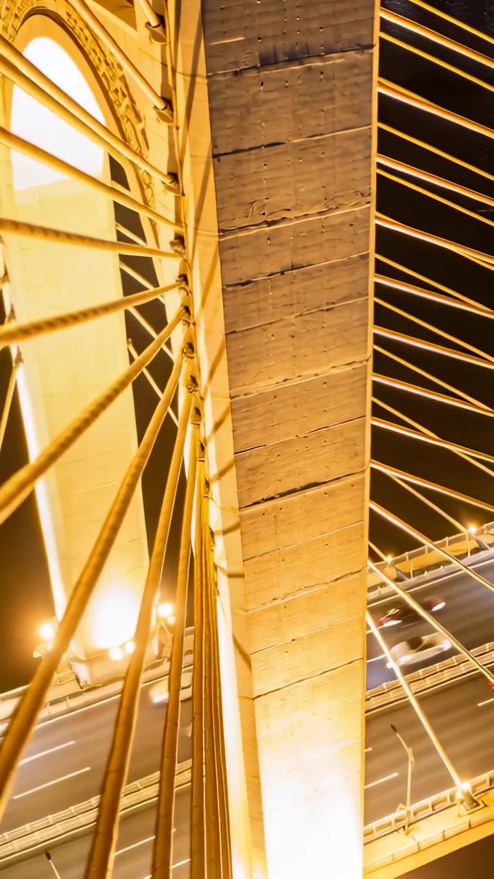 Video verticale: Telecamera rotante che rivela un pilone di notte su un ponte, mostrando cavi e scie luminose