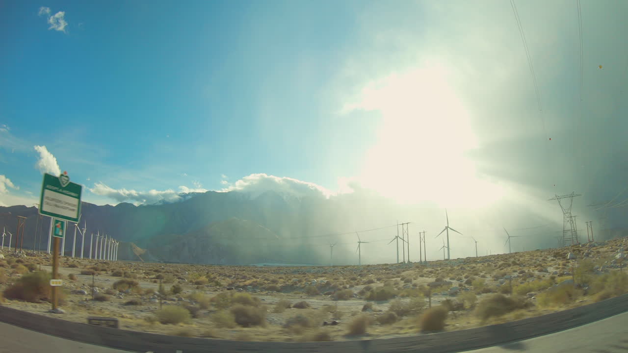 Sun Rays shine over the desert as wind turbines spin at the base of a mountainside. Located in Joshua Tree California.