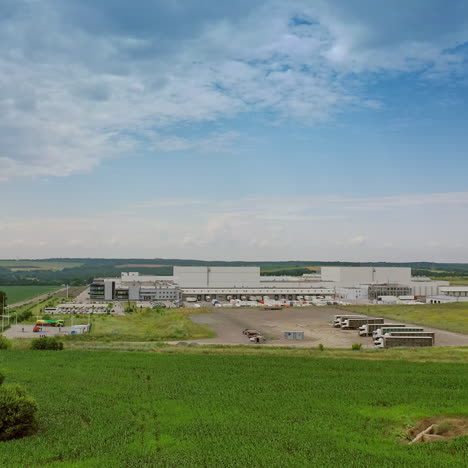 exterior of industrial complex in the countryside. modern buildings with parking for trucks among green fields under blue sky in summer.