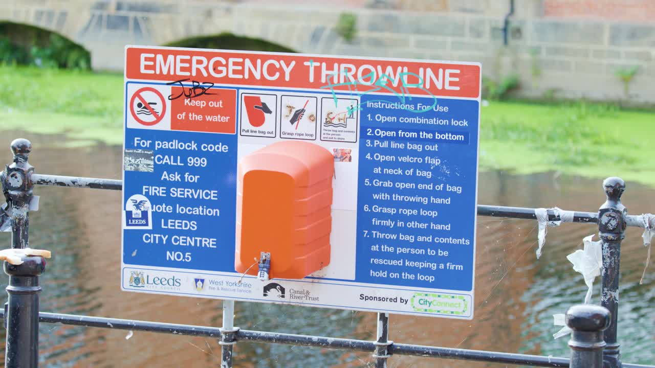 Static shot of emergency throwline safety sign near riverside, bright daylight, outdoor urban environment
