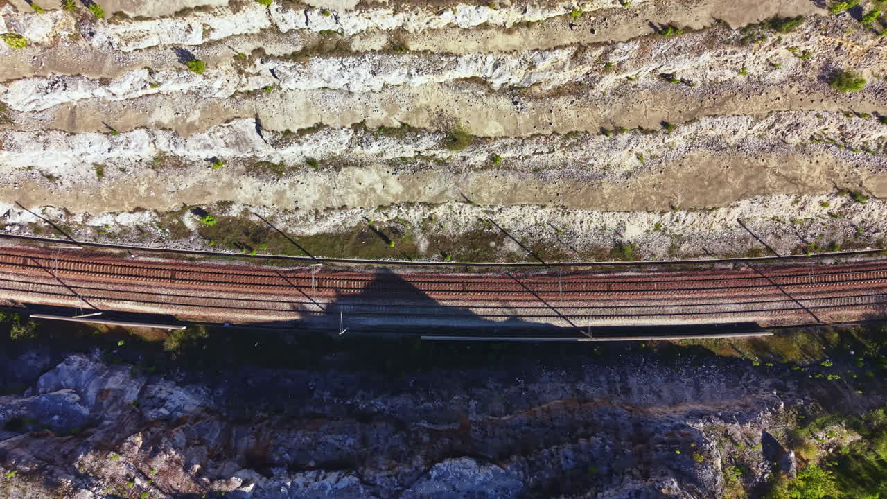 Train tracks run alongside rocky terrain in a remote area during daylight, showing the contrast between nature and human-made paths