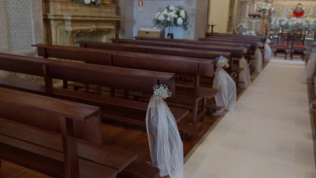 Navata della chiesa con panche in legno decorate con tulle bianco e fiori, che conduce verso l'altare con un tappeto bianco