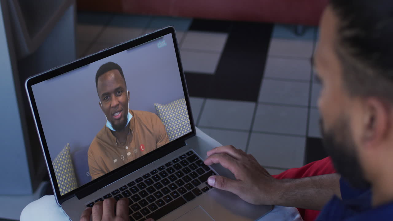 hombre afroamericano teniendo una videollamada con un colega de oficina masculino en una computadora portátil en casa