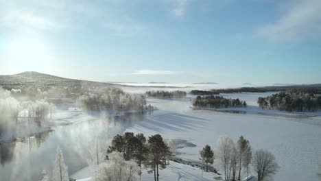 Drone-shot-flying-over-frozen-lake-with-mist-drifting-over-it-and-vast-forests-and-hills-in-the-distance-in-Northern-Sweden