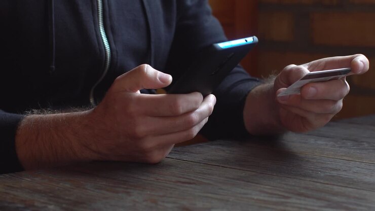Businessman in a black hoodie making online payment with credit card and smartphone, online shopping