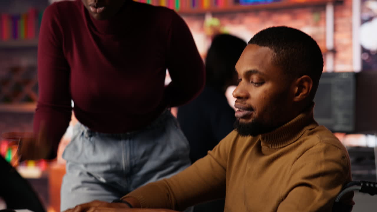 Man with disability typing on PC and chatting with coworker