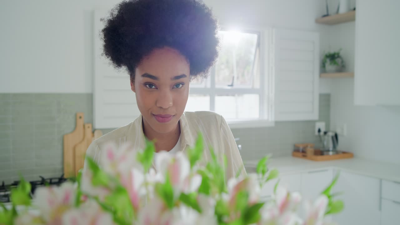Erwachsene afrikanische Frau beugt sich in der Küche zu einem großen Blumenstrauß, vom Duft angezogen, riecht und lächelt