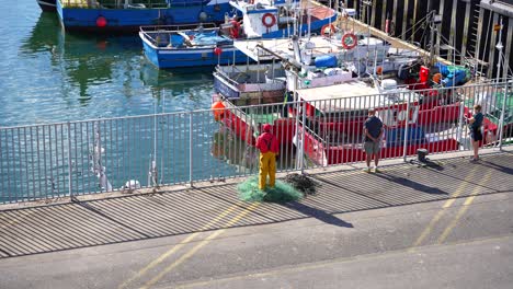 fisherman collects green nets on the santona port dock as boats sit in the calm cantabrian sea