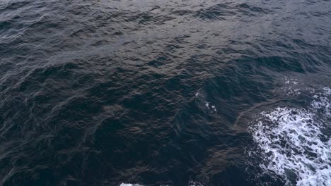 Scenic-View-Of-Waves-Splashing-Away-From-A-Sailing-Boat-In-The-Sea---high-angle-slowmo-shot