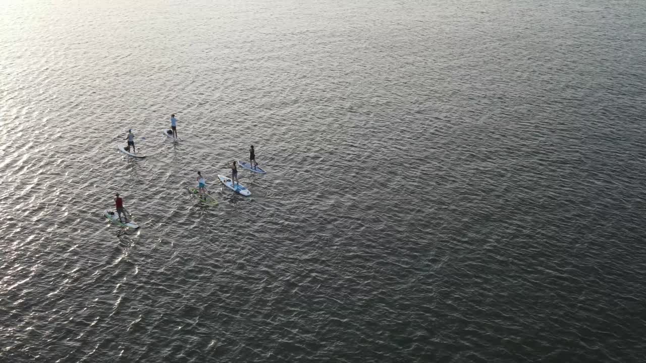 gente haciendo surf de remo en el mar azul con olas tranquilas durante la puesta de sol
