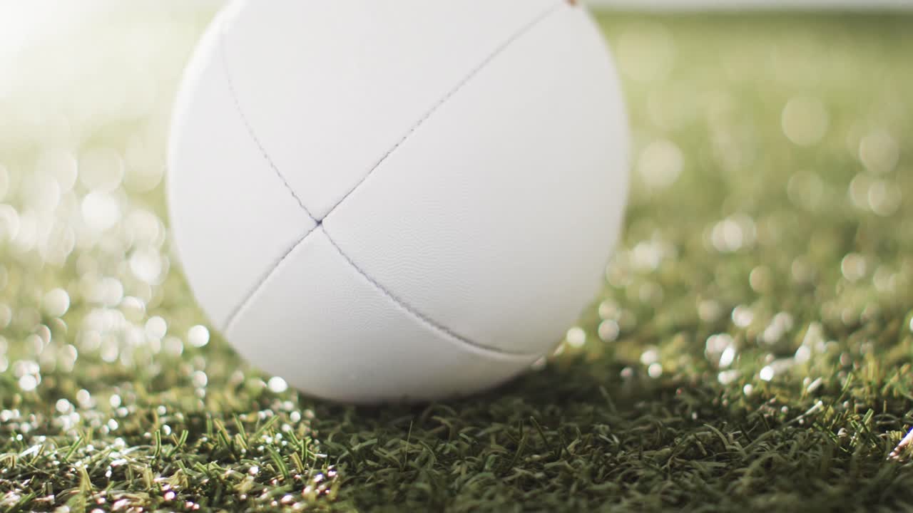 weißer rugbyball auf sonnendurchleuchtetem gras mit kopierraum, langsame bewegung