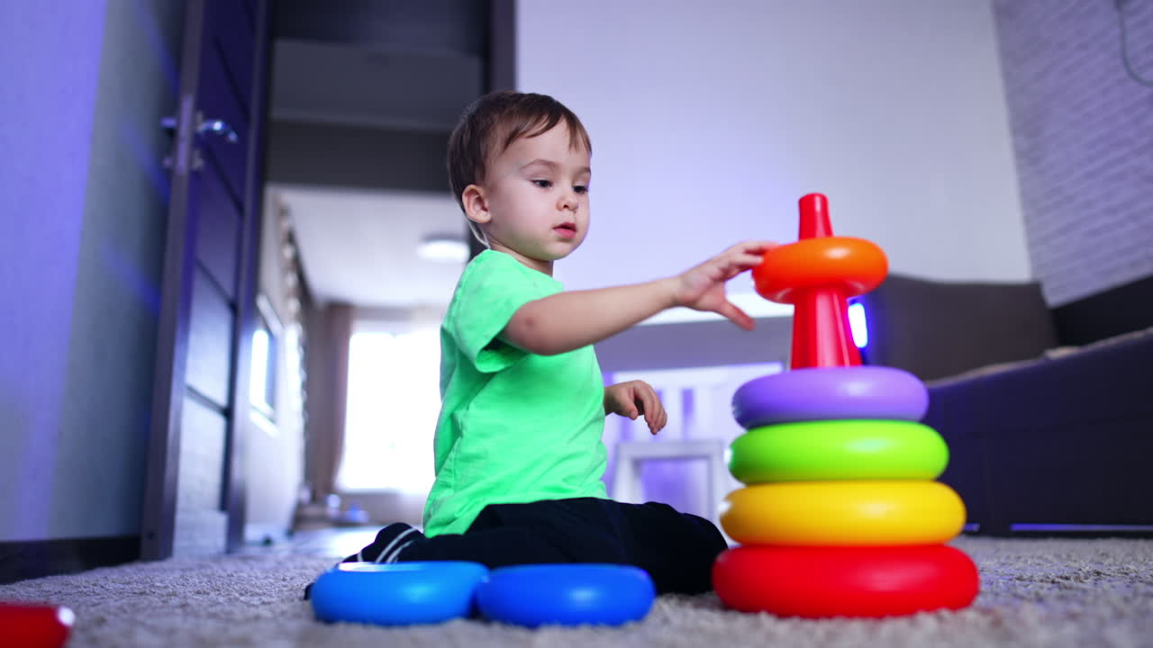 Baby boy playing with colorful pyramid. Child playing on the floor at home. Low angle view.
