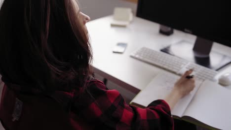 Backside-footage-of-unrecognizable-female-brunette-writing-something-on-paper.