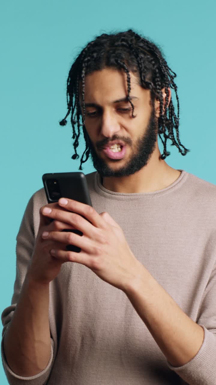 Video verticale. Un uomo manda un messaggio a un amico usando uno smartphone, ridendo per una barzelletta divertente, sfondo da studio
