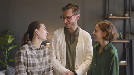 grupo de tres personas posando y sonriendo a la cámara mientras están de pie en una sala de estar moderna en casa