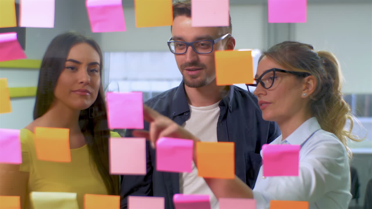 Team of two women and a man with glasses in the office discussing plans on stickers. New idea concept. Shot through glass