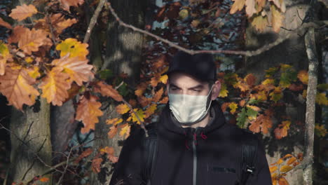 male tourist wearing face mask in forest walking towards camera, covid pandemic symbolism, middle front closeup shot