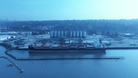 ukrainian freighter docked loading wheat grains from canadian port surrey bc aerial drone hold overlooking commercial vehicles working with staff sunny summer day clear sky silo mylar-type bags cans