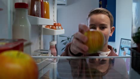niño adolescente mirando dentro del refrigerador y alcanzando una manzana