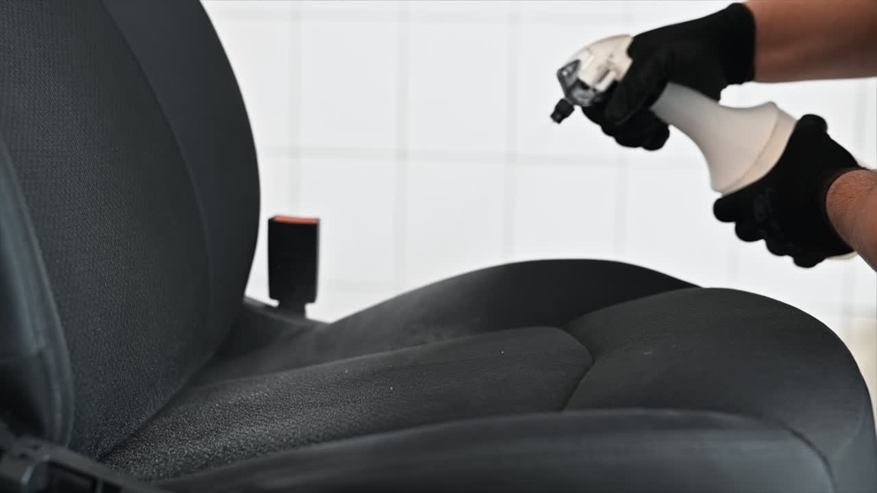 Working cleaner at car wash. Cleaning a seat using a spray with chemical solution. Slow motion