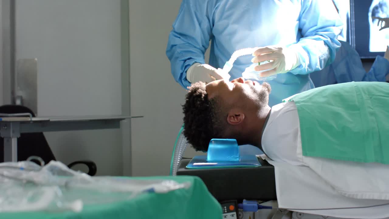 Chirurgo uomo afroamericano che somministra l'anestesia a un paziente in sala operatoria, al rallentatore