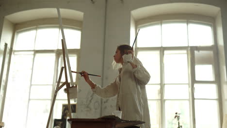 inspired woman working in art studio. female painter painting on canvas indoors.