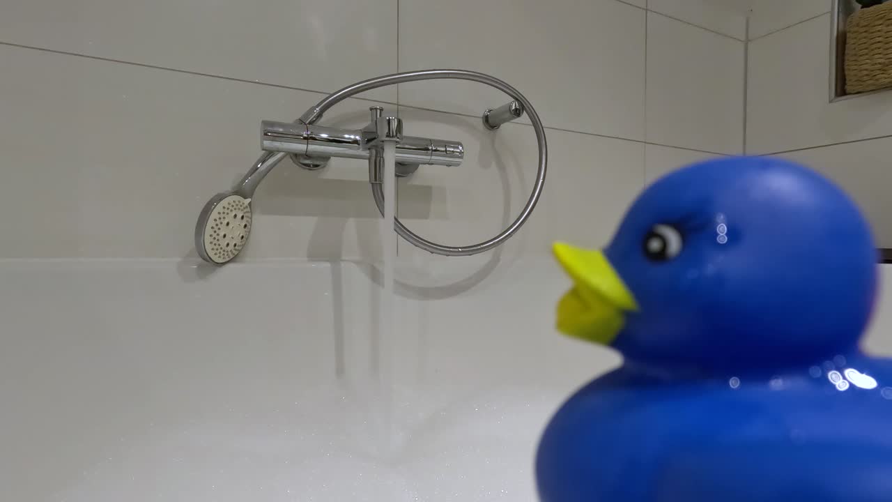 Blue rubber duck looking at the bathtub being filled.