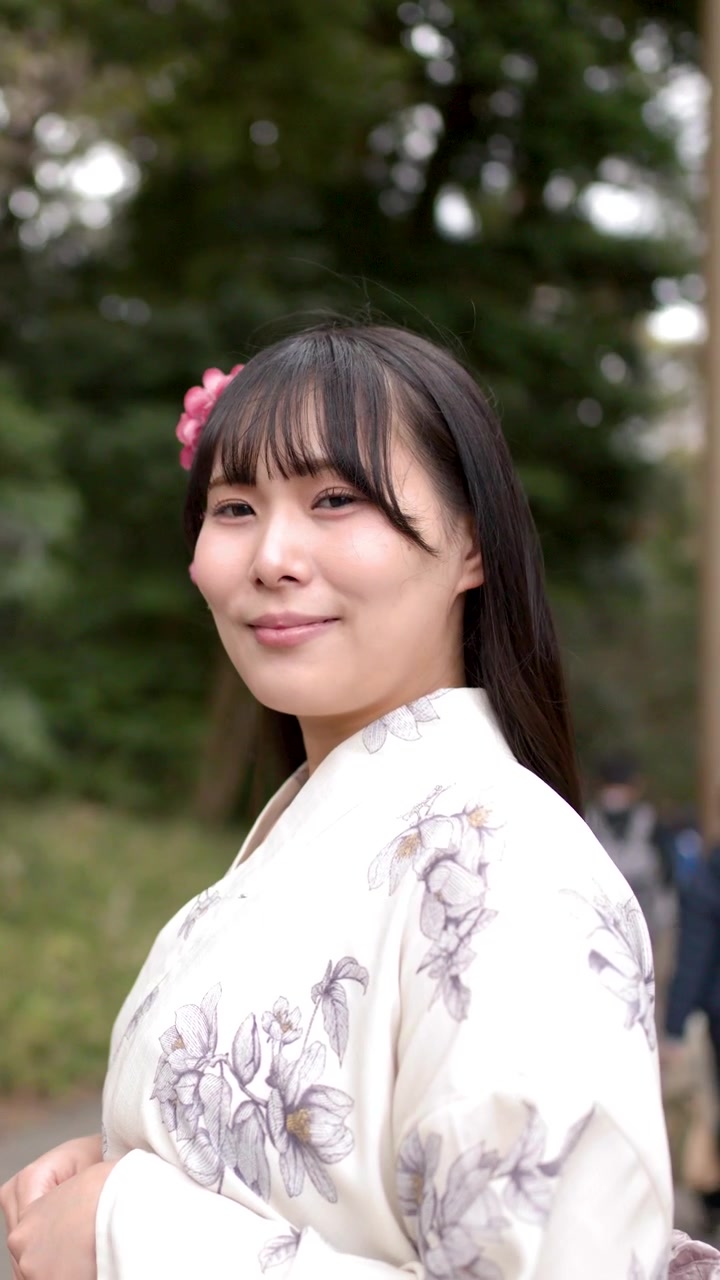 Una donna giapponese sorridente indossa un kimono floreale mentre si trova davanti a un torii.