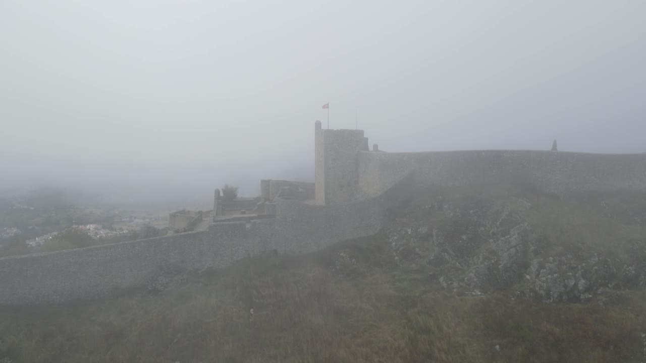 un dron gira alrededor de una bandera en el castillo de marvão en una espesa niebla