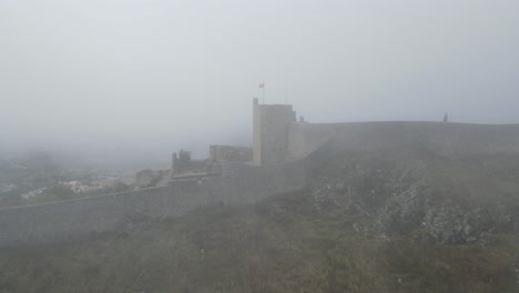 Eine-Drohne-Dreht-Sich-In-Dichtem-Nebel-Um-Eine-Fahne-Auf-Der-Burg-Von-Marvão