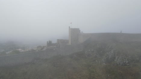 a drone rotates around a flag on the castle of marvão in thick mist