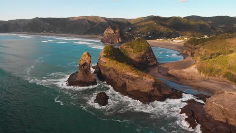 Hohe-Wellen-Spülen-Die-Klippen-Des-Piha-Strandes,-Die-Zur-Goldenen-Stunde-In-Warmen-Farben-Gestrichen-Sind