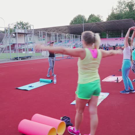 group of women doing workout on the modern stadium. young female trainer shows fitness exercises to women in the outdoor sports ground.