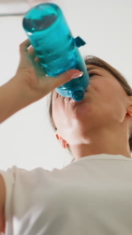 mujer toma una botella de agua mientras corre. mujer enérgica rejuvenece con agua pura durante el entrenamiento en la máquina de ejercicio en el club tiro de bajo ángulo