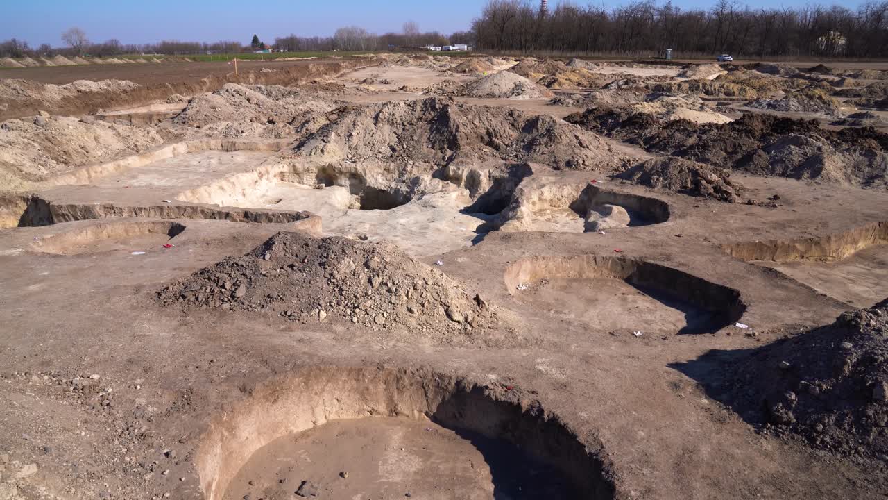 High angle establishing view of archaeology dig site marked with pits, dirt mounds