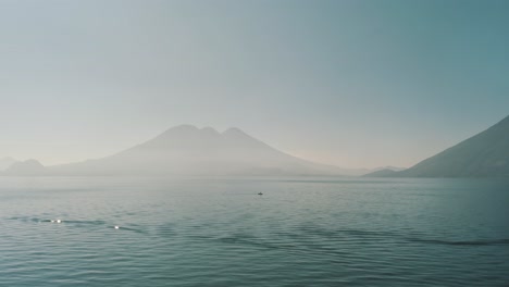 drone aerial view, a man on a boat on lake atitlan and volcanoes surrounding it in lake atitlan, guatemala