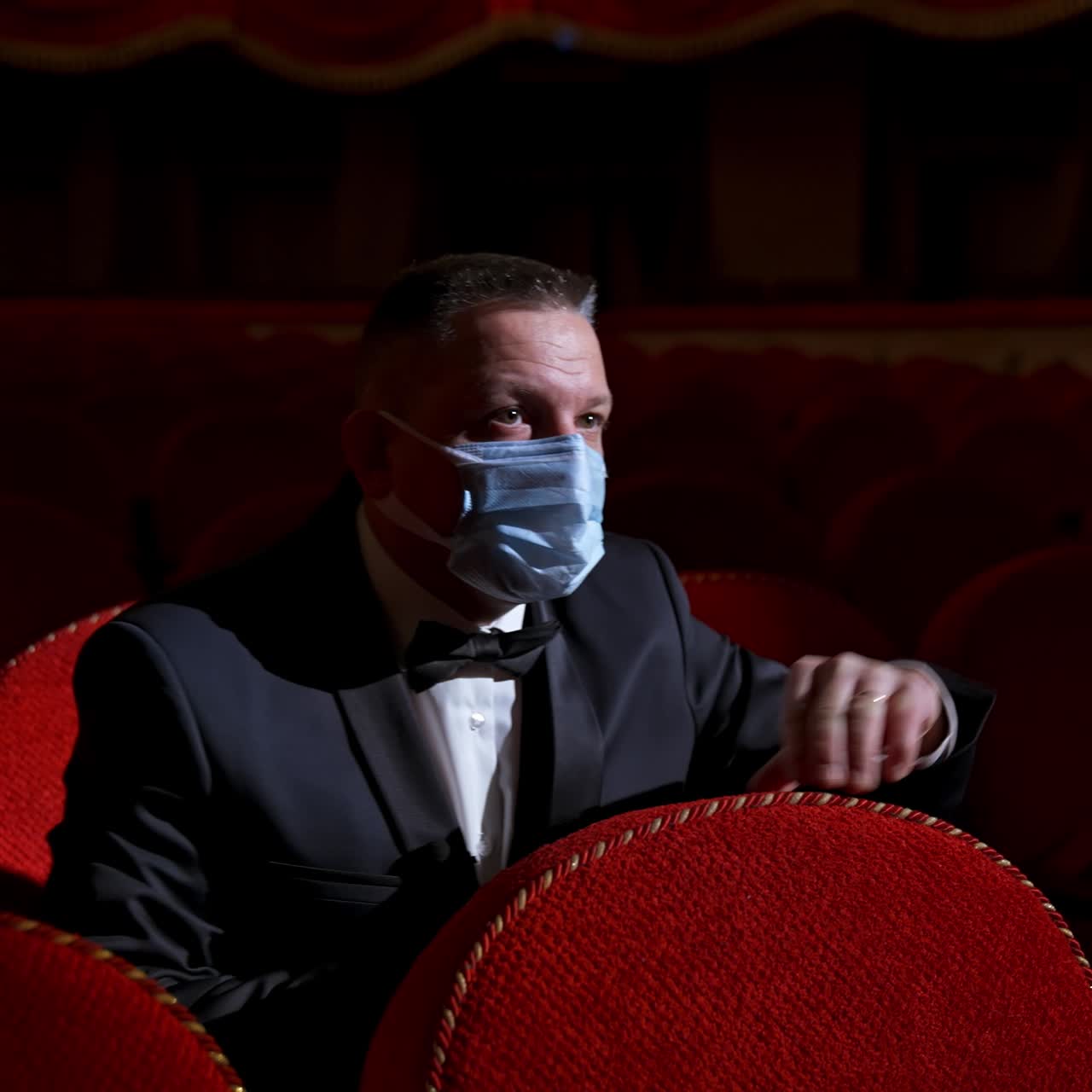 Theater hall after pandemic. Male in medical mask sits alone in empty hall with red seats. Covid-19 concept