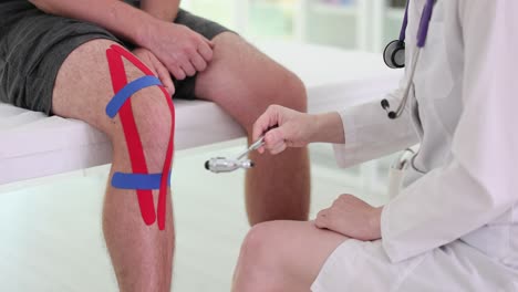 doctor examining patient's knee with reflex hammer and kinesiology tape