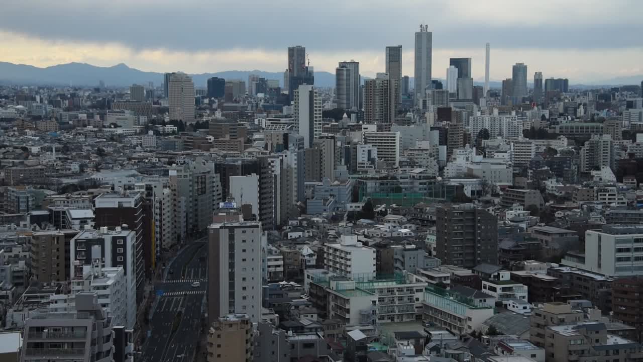 Expansive view of Tokyo cityscape with dense low-rise buildings leading into tall skyscrapers under cloudy sky at dusk