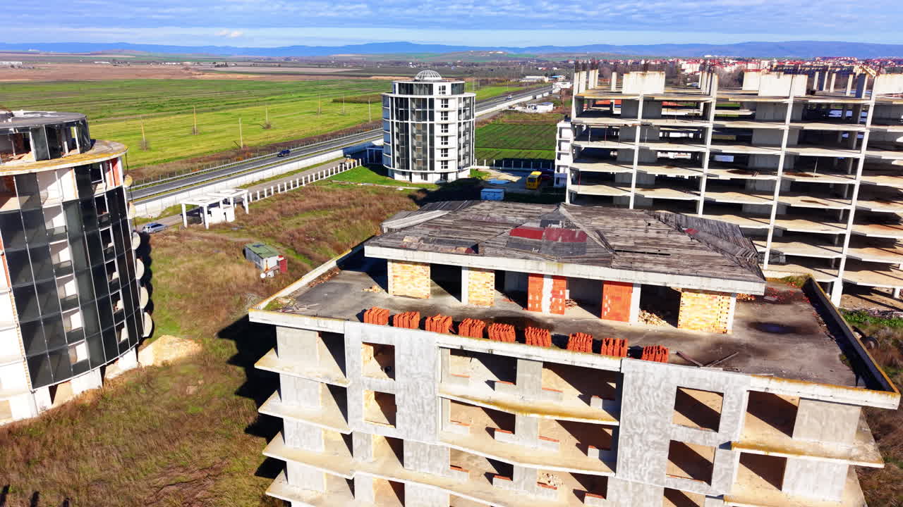 Ansammlung unfertiger Betongebäude mit Glaselementen, umgeben von überwucherter Vegetation und einem zentralen Wasserbecken. Verlassene Baustelle. Luftaufnahme von oben