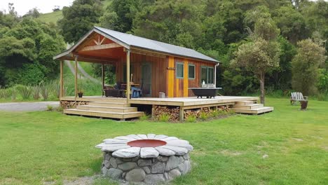 a wood cabin in nature with a stone fire pit on the lawn in new zealand